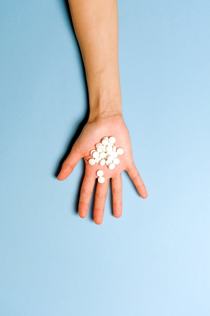 gallery-04 A hand holding white pills on a light blue background symbolizing medication and healthcare.